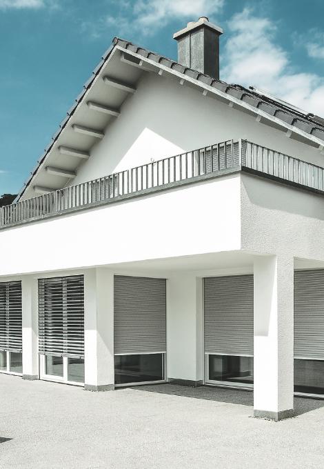 Pointed roof single-family home with balcony and nearly closed roller shutters by dayligth