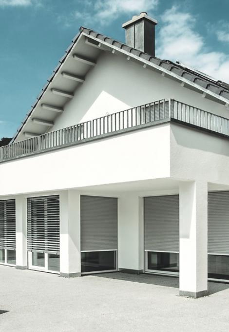 Pointed roof single-family home with balcony and nearly closed roller shutters by dayligth