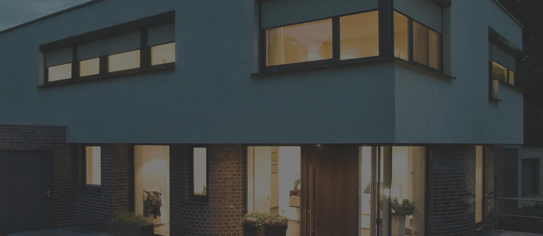 Home in the twilight with interior lighting and half closed roller shutters