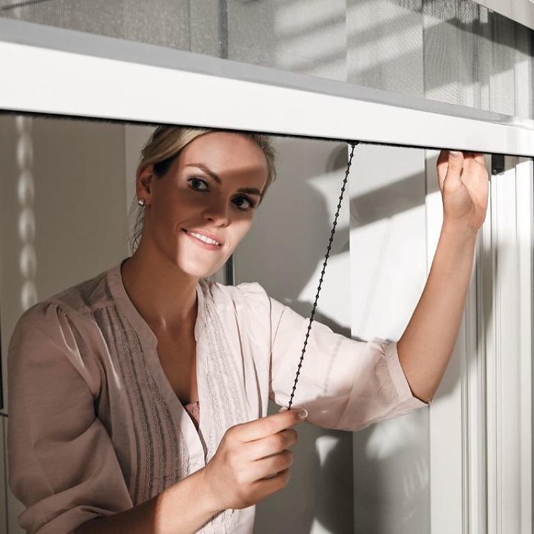 Exterior view, woman closes insect screen roller shutter with open window