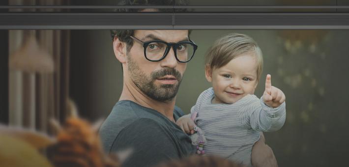 Man is standing in front of the window with a baby in his arms