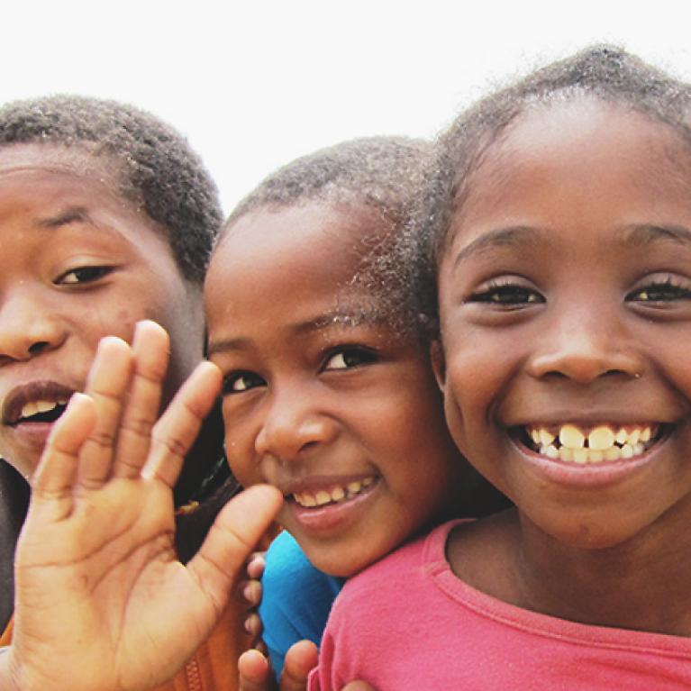 Auxilium e.V. Image section, three coloured children laugh and wave to the camera