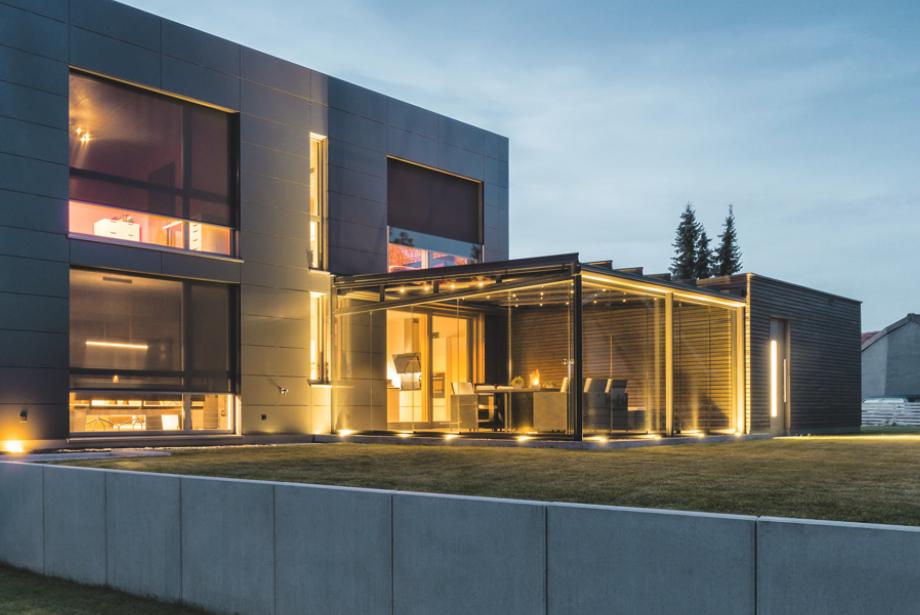 Modern house with interior lighting and lowered front-mounted textile screens in the twilight
