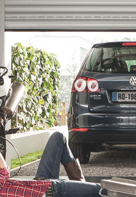 Woman lays on the floor and screws at her motorcycle in the garage, a car stands in the front
