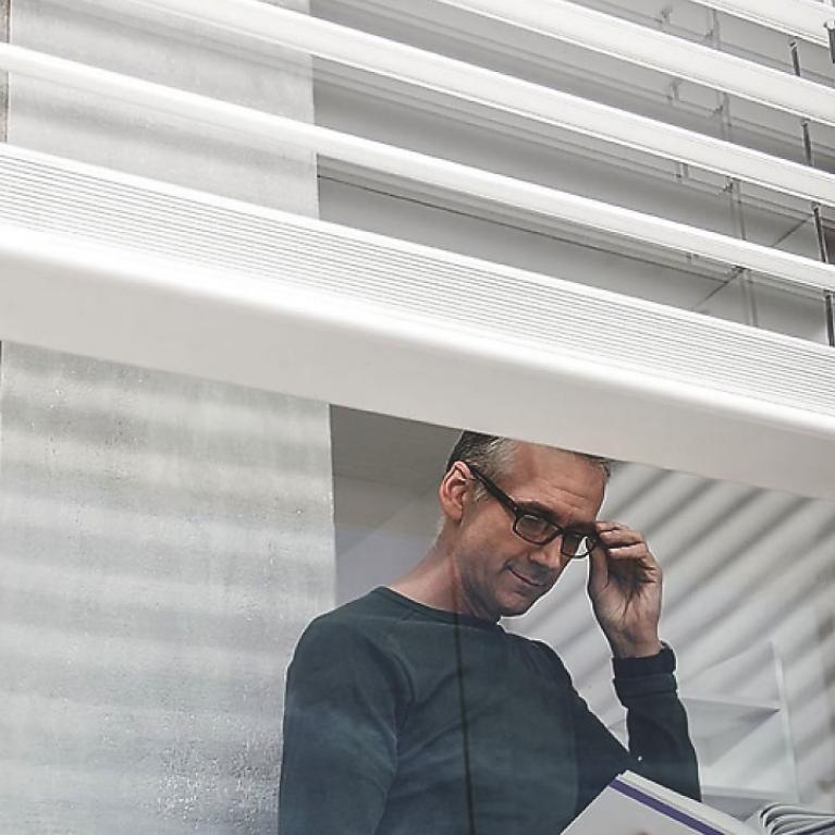 Man reads book behind window, detailed view, external venetian blinds, open