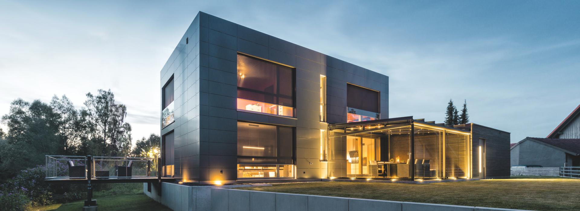Modern house with interior lighting and lowered front-mounted textile screens in the twilight