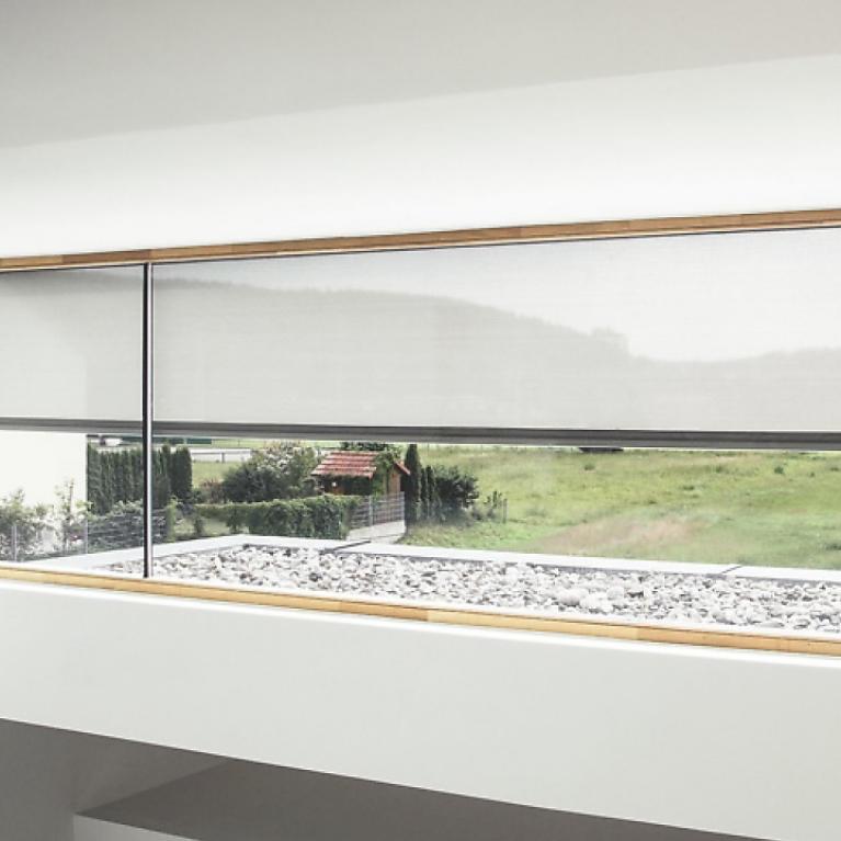 Detailed view window front from the inside with half lowered textile screens by daylight