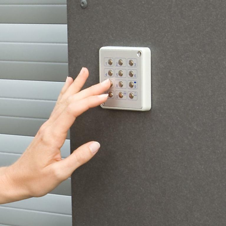 ROMA Code Box Close-up Wall besides garage door with hand tapping on the code box