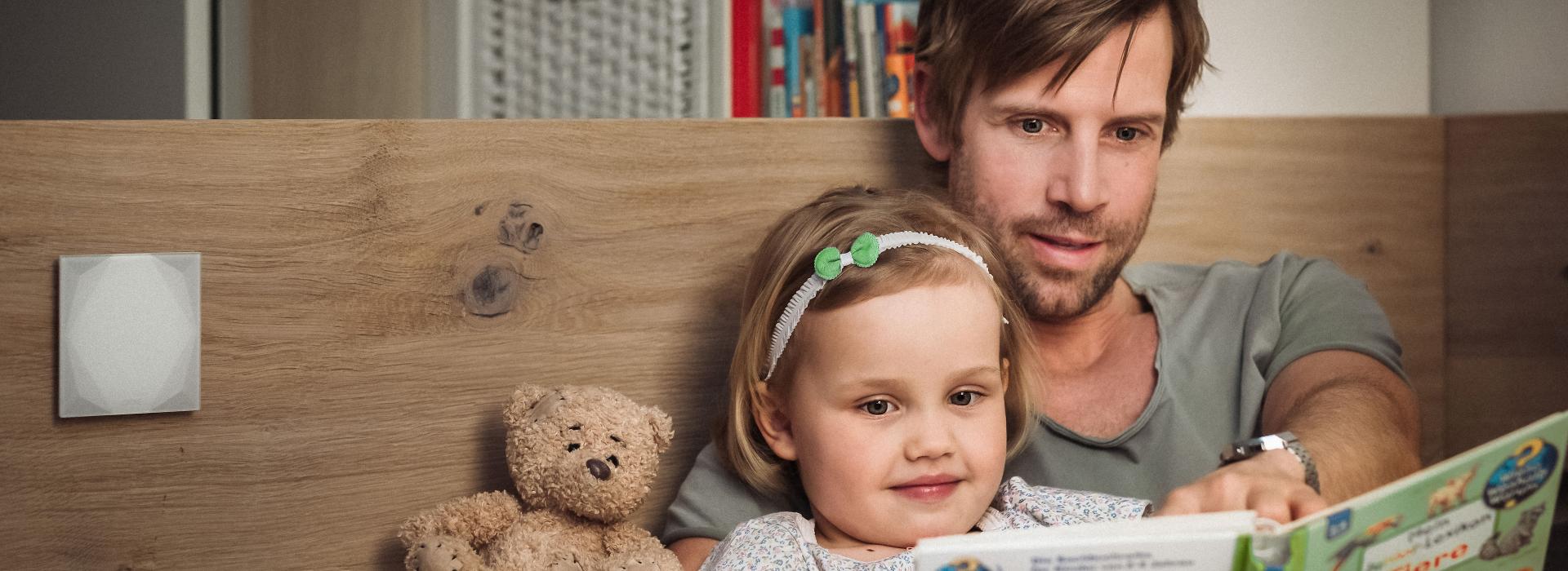 Father sits in bed with his daughter reading a book