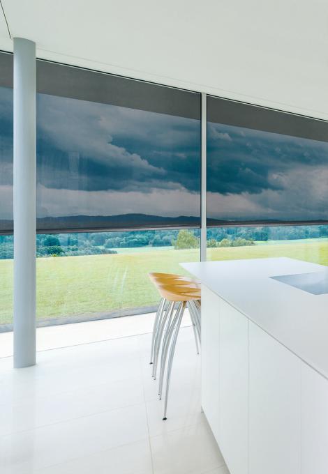 Modern white kitchen with half closed textile screens, view to the outside