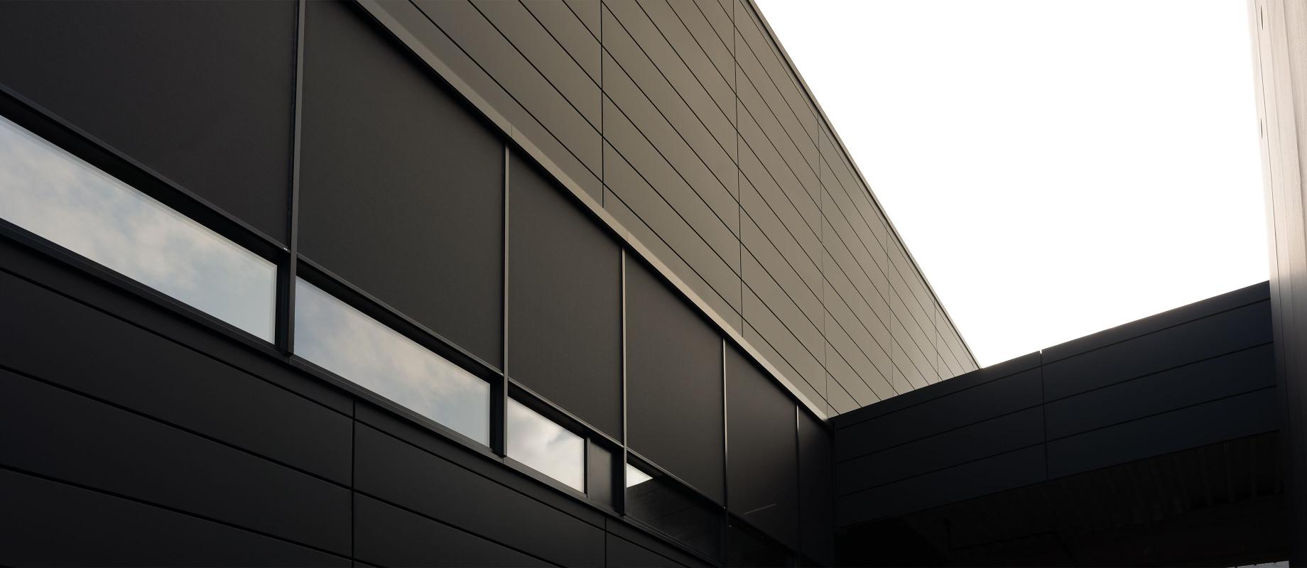 Dark factory façade with large windows and grey textile screens